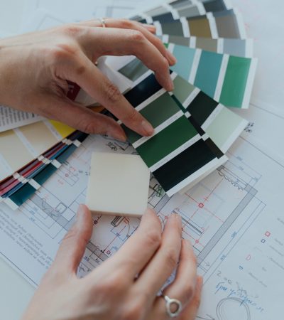 Hands selecting color samples over architectural plans for interior design.